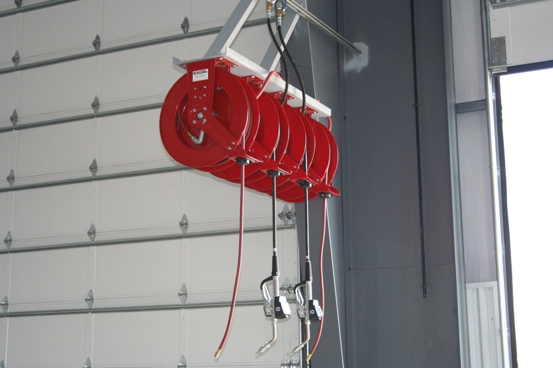 Multiple red hose reels mounted to a ceiling in a workshop with dispensing nozzles hanging down.