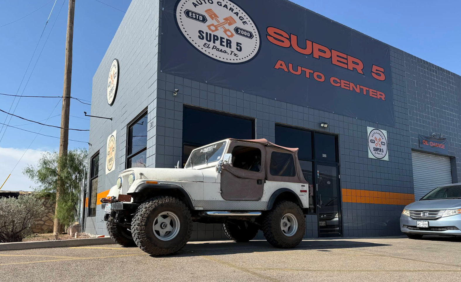 White off-road Jeep parked outside Super 5 Auto Center on a sunny street. | Super 5 Auto Center