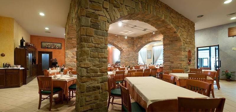 Accogliente sala da pranzo del ristorante con arco in pietra, tavoli in legno e luci calde.