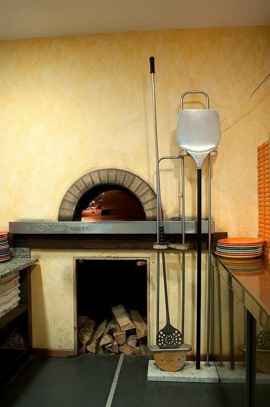 Forno per pizza a legna con pala a manico lungo e contenitore bianco in una cucina rustica
