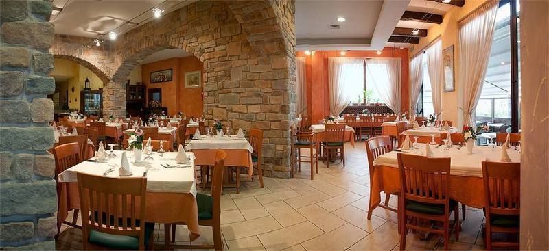 Elegante sala da pranzo del ristorante con arco in pietra, tovaglie bianche e calda illuminazione soffusa.