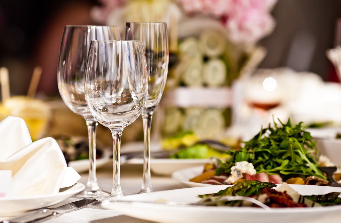 Elegante tavola apparecchiata con bicchieri da vino, tovaglioli piegati e pietanze servite in una delicata composizione floreale.