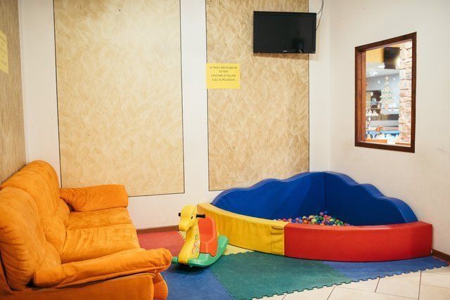 Sala giochi interna con sedie arancioni, una piscina di palline blu e gialla e una TV montata a parete.