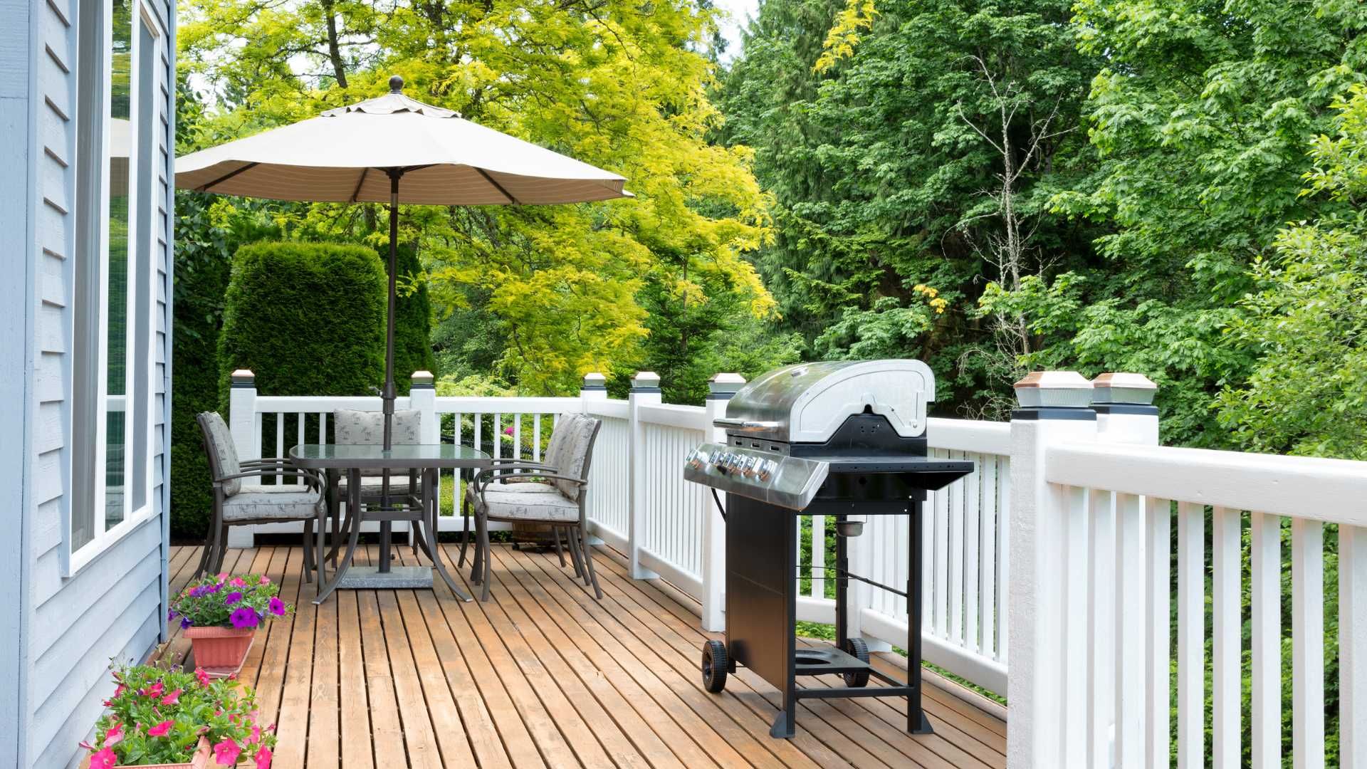 Wooden deck with patio table, umbrella, grill, and white railing overlooking green trees