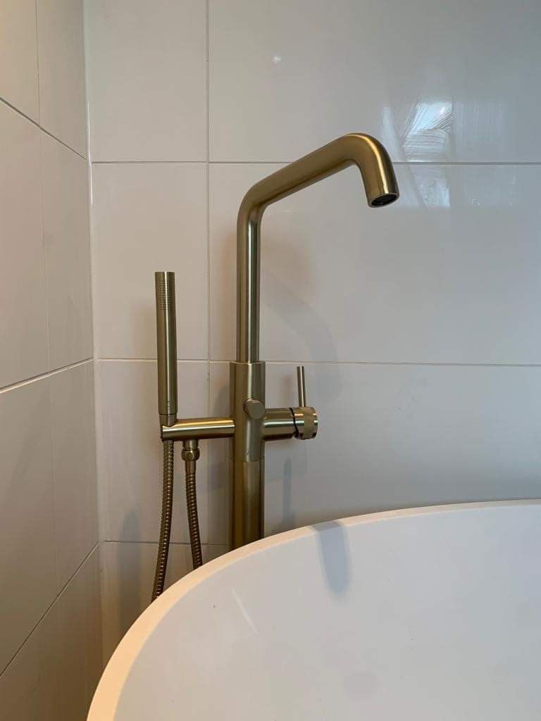 Brass bathtub faucet with handheld shower beside a white tub and tiled wall