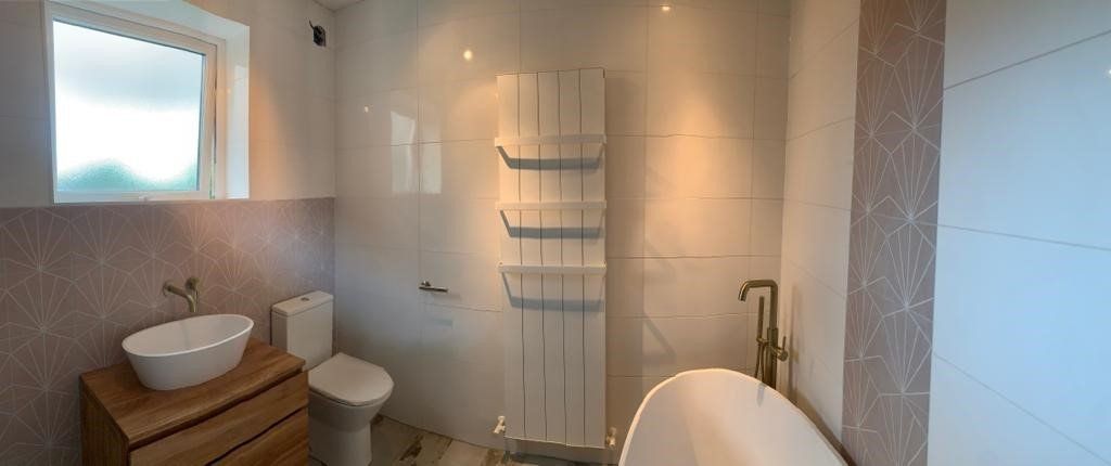 Modern bathroom with wood vanity, white sink, towel ladder, and bathtub