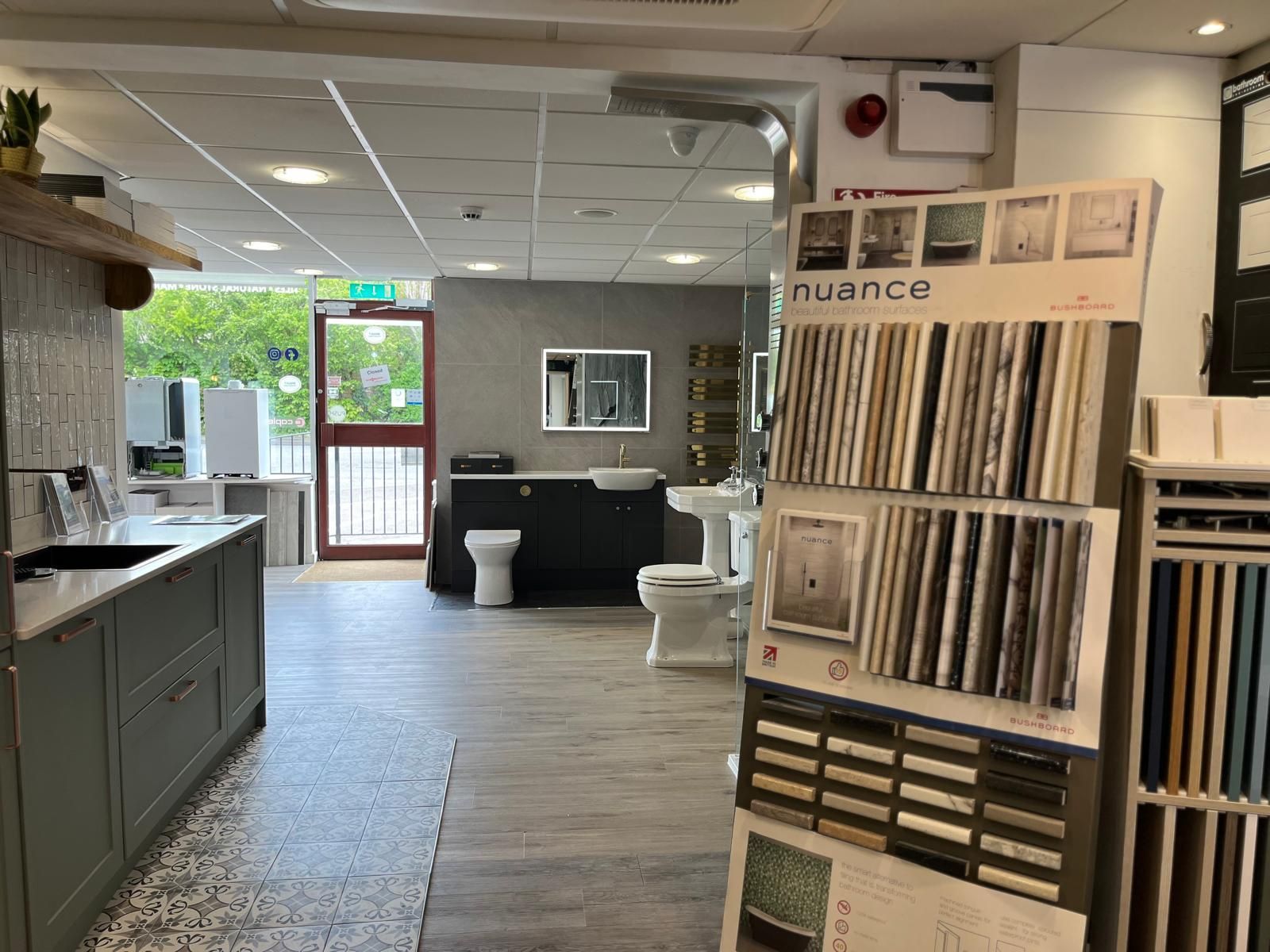 Modern showroom interior with a tile display wall, kitchen counter, and seating near a glass entrance.