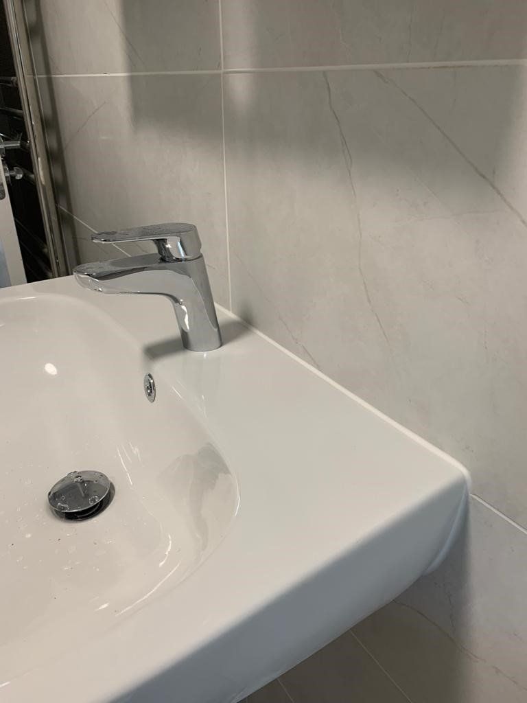 White bathroom sink with chrome faucet against beige tiled wall.