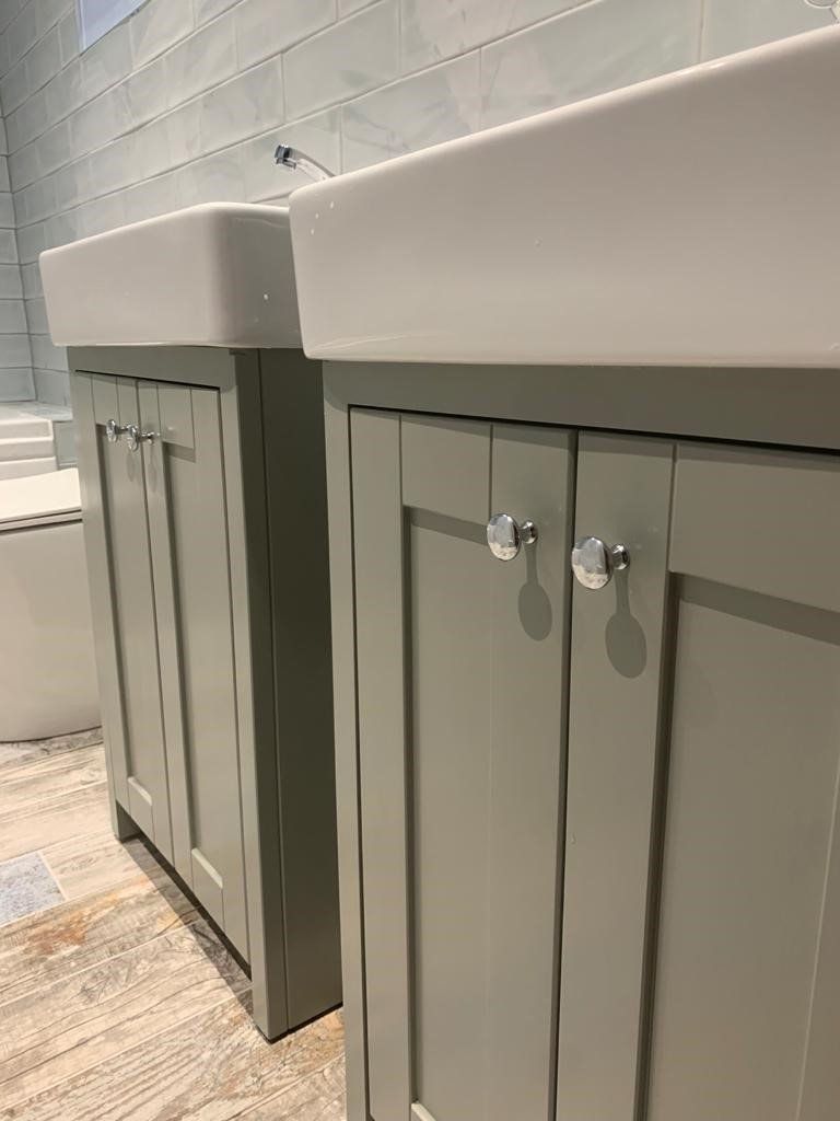 Gray bathroom vanity cabinets beside a white sink with silver knobs on a tiled floor
