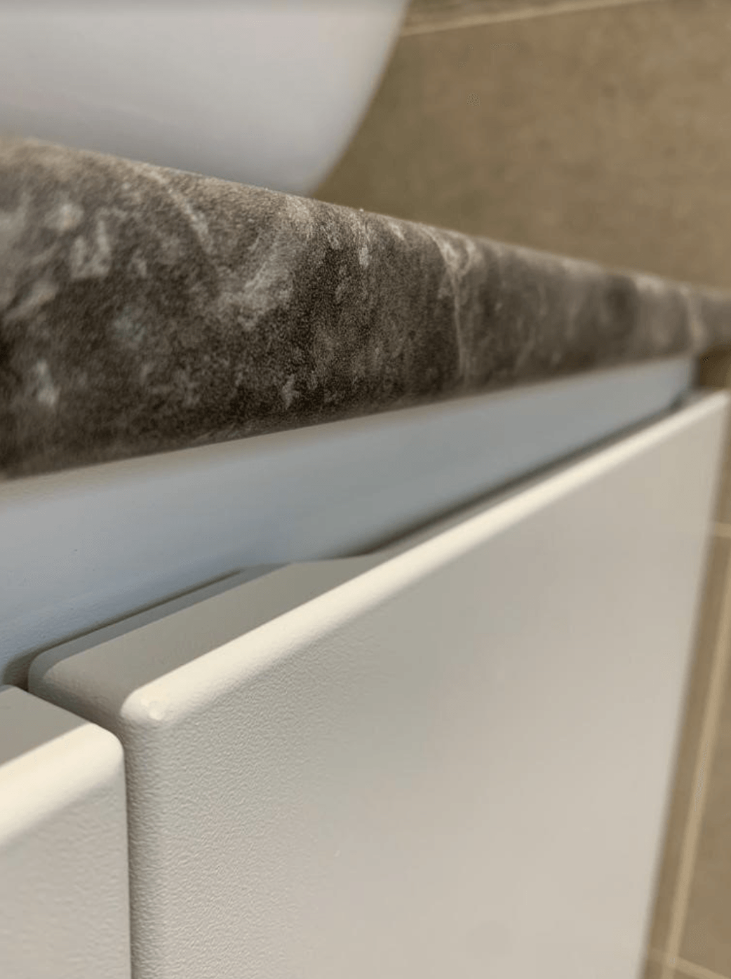 White towel rail mounted under a dark marble countertop beside beige bathroom tile.