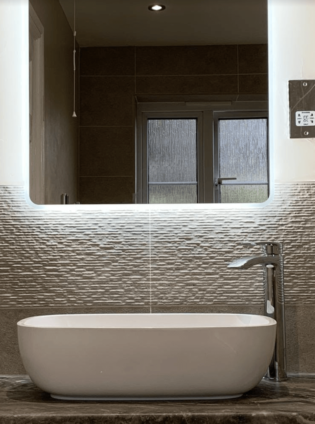 Modern bathroom with a freestanding white tub, textured wall, mirror, and dark tile accents.