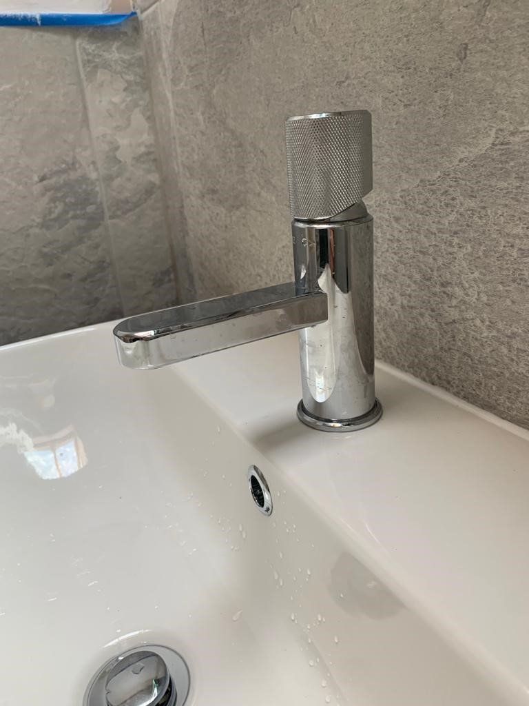 Chrome faucet with a flat lever over a white sink against a gray wall.