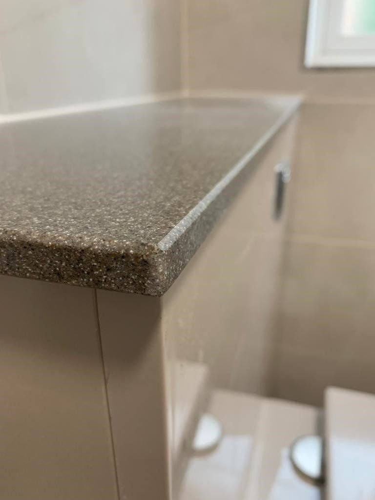 Close-up of a speckled countertop edge above a bathroom sink and mirror in soft light