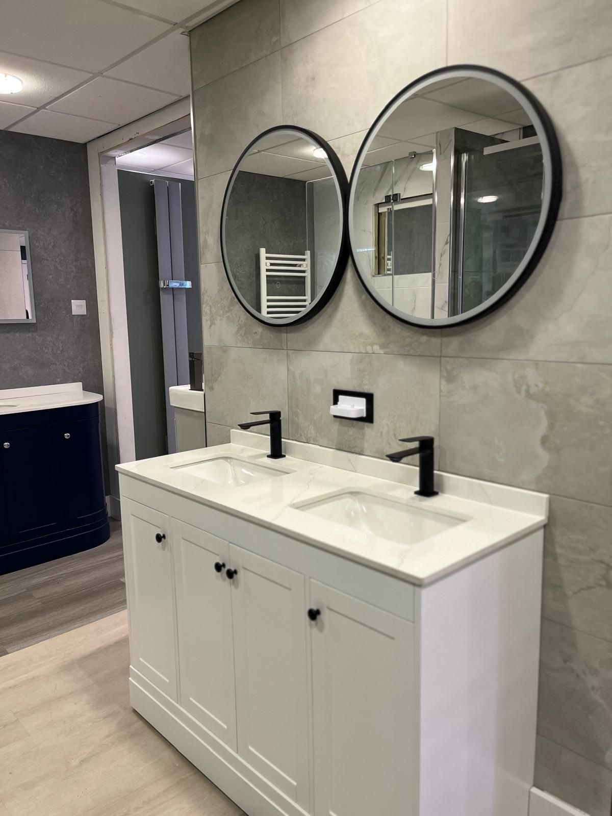 Modern bathroom vanity with two round mirrors, white cabinet, and black faucets in a gray-tiled room
