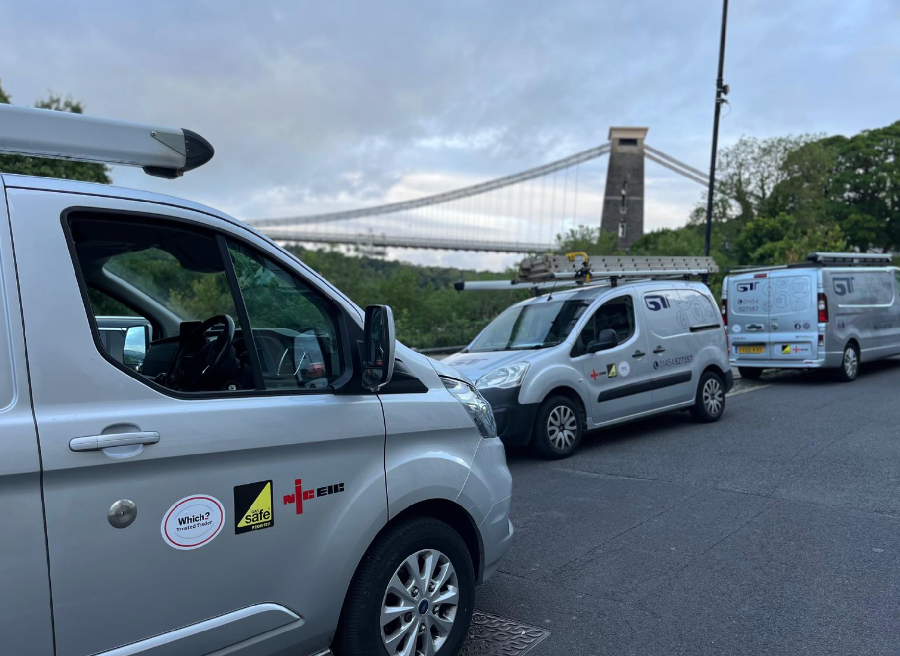 Silver service vans parked near the suspension bridge in a city street.