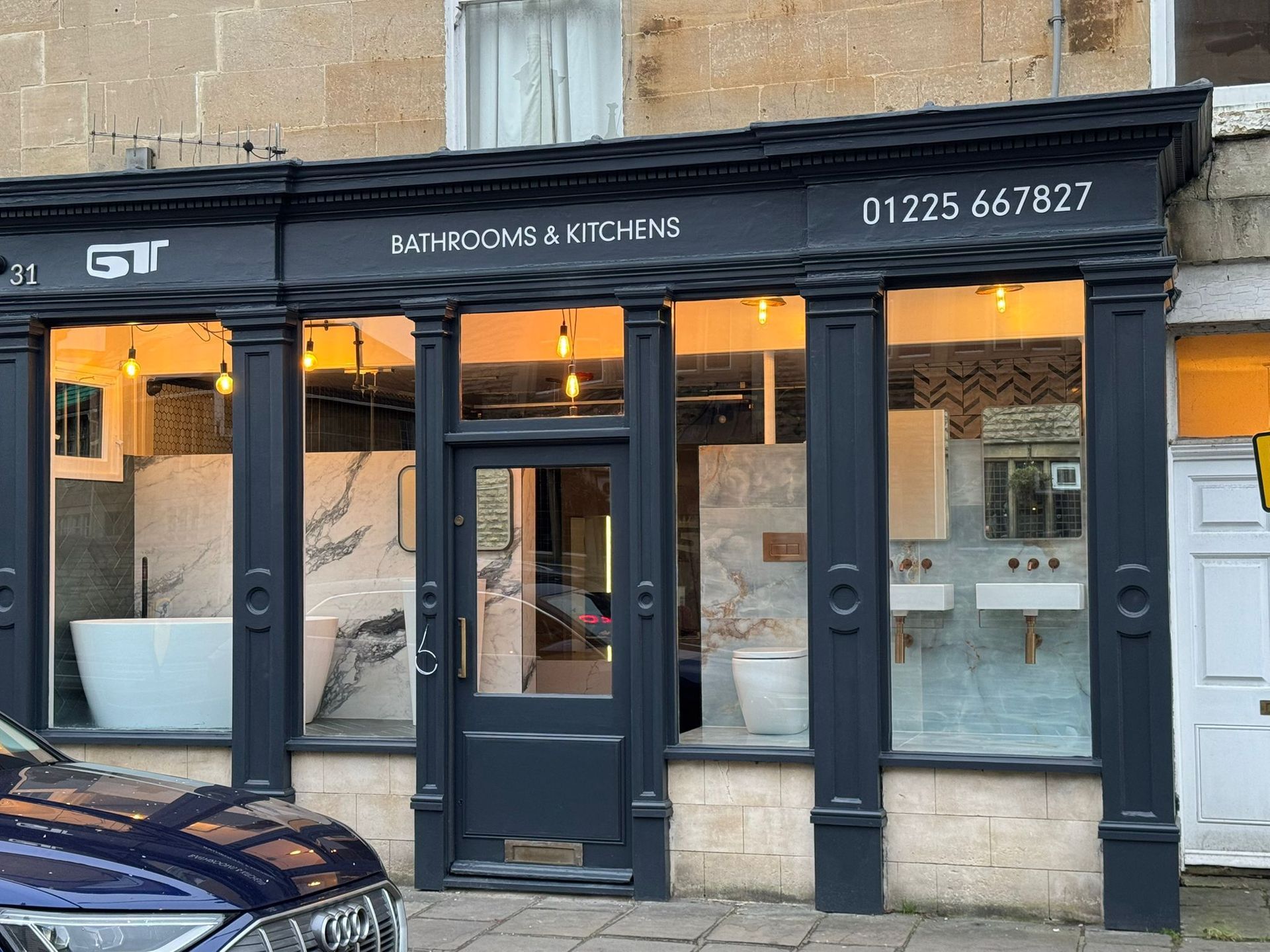 Storefront of a kitchen showroom with black facade, glass windows, and warm interior lighting on a stone building.
