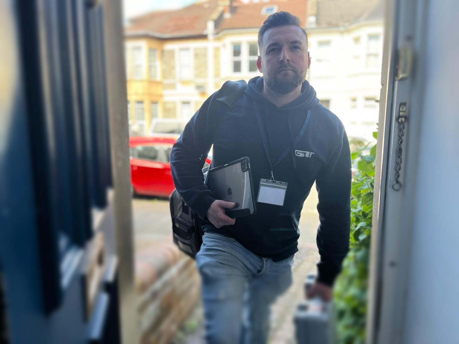Man in a black jacket carrying a folder walks up to a doorway from outside.