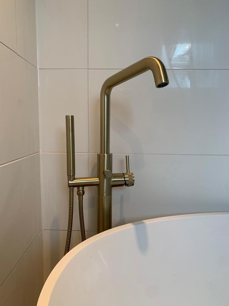 Brass bathtub faucet and shower wand beside a white tub in a tiled bathroom