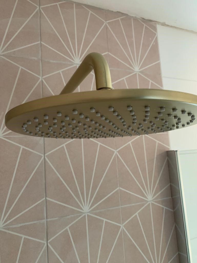 Round brass shower head against patterned bathroom wall tiles