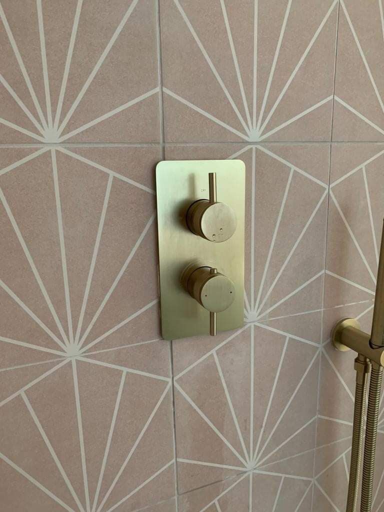 Wall-mounted beige control panel with two round knobs on patterned wallpaper, beside a hanging cord