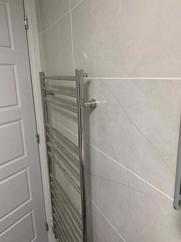 Chrome towel radiator beside a white paneled door in a tiled bathroom
