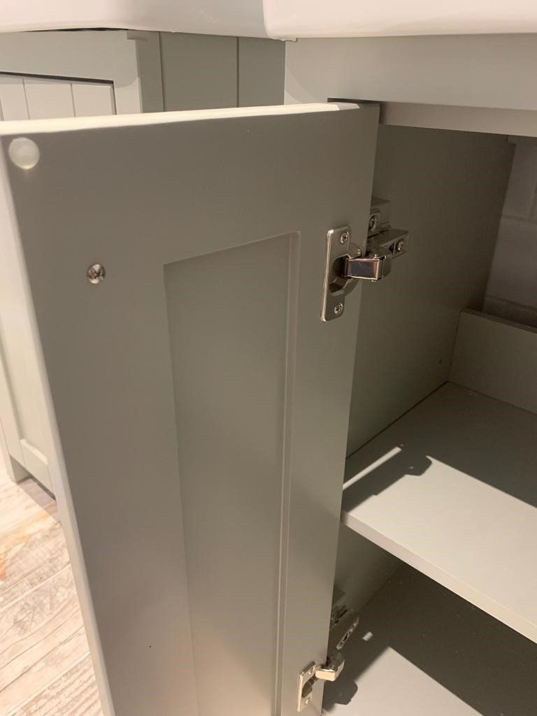 Open gray bathroom stall door with metal hinges and a shelf visible inside