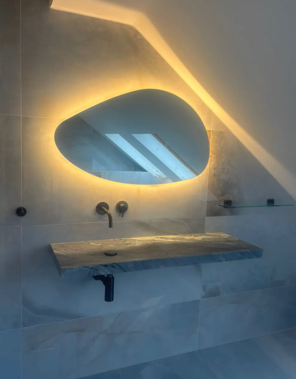 Modern bathroom vanity with oval backlit mirror above a floating stone sink.