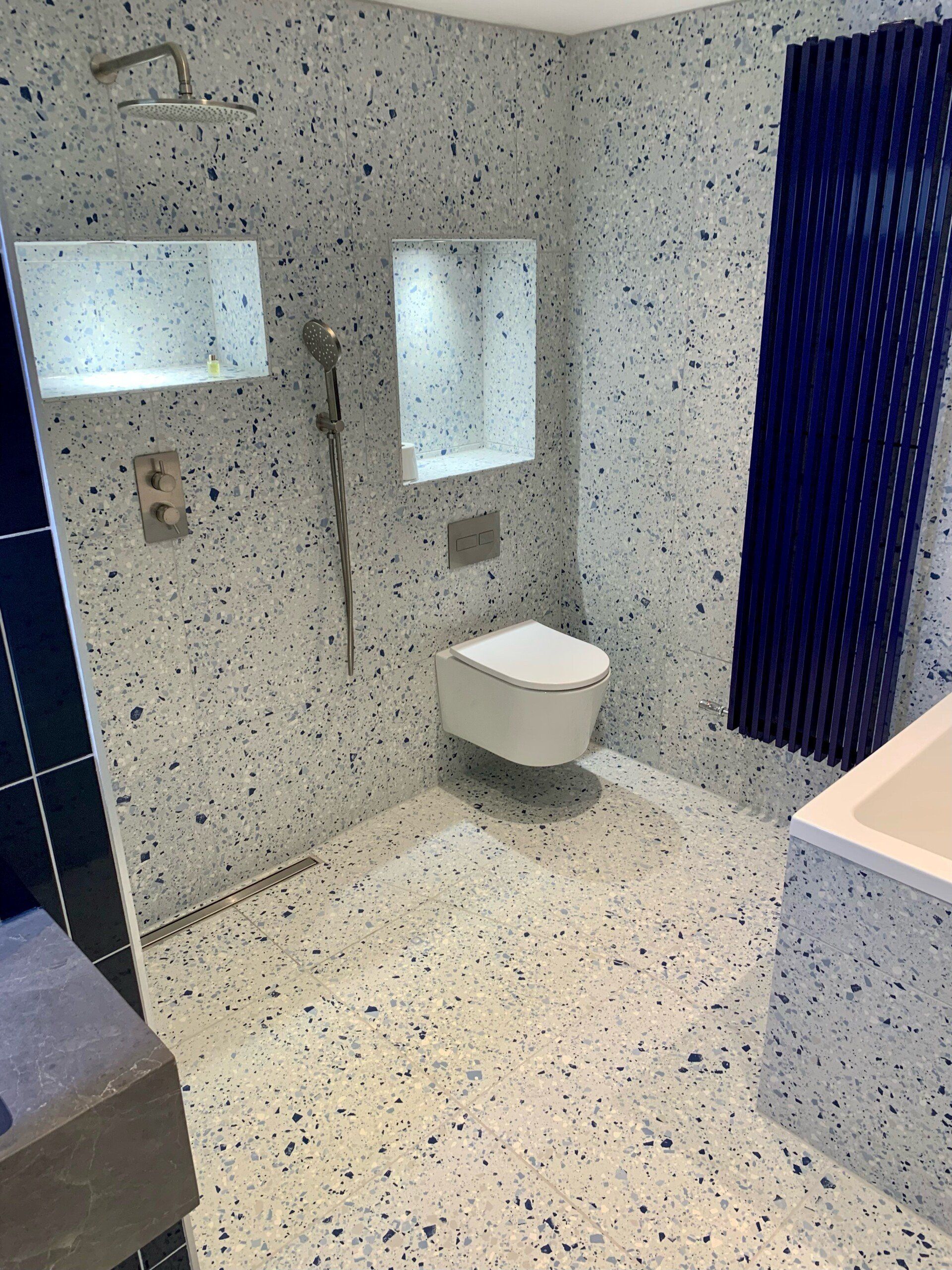 Modern shower room with speckled tile walls, wall mirror, toilet, and blue shower curtain.