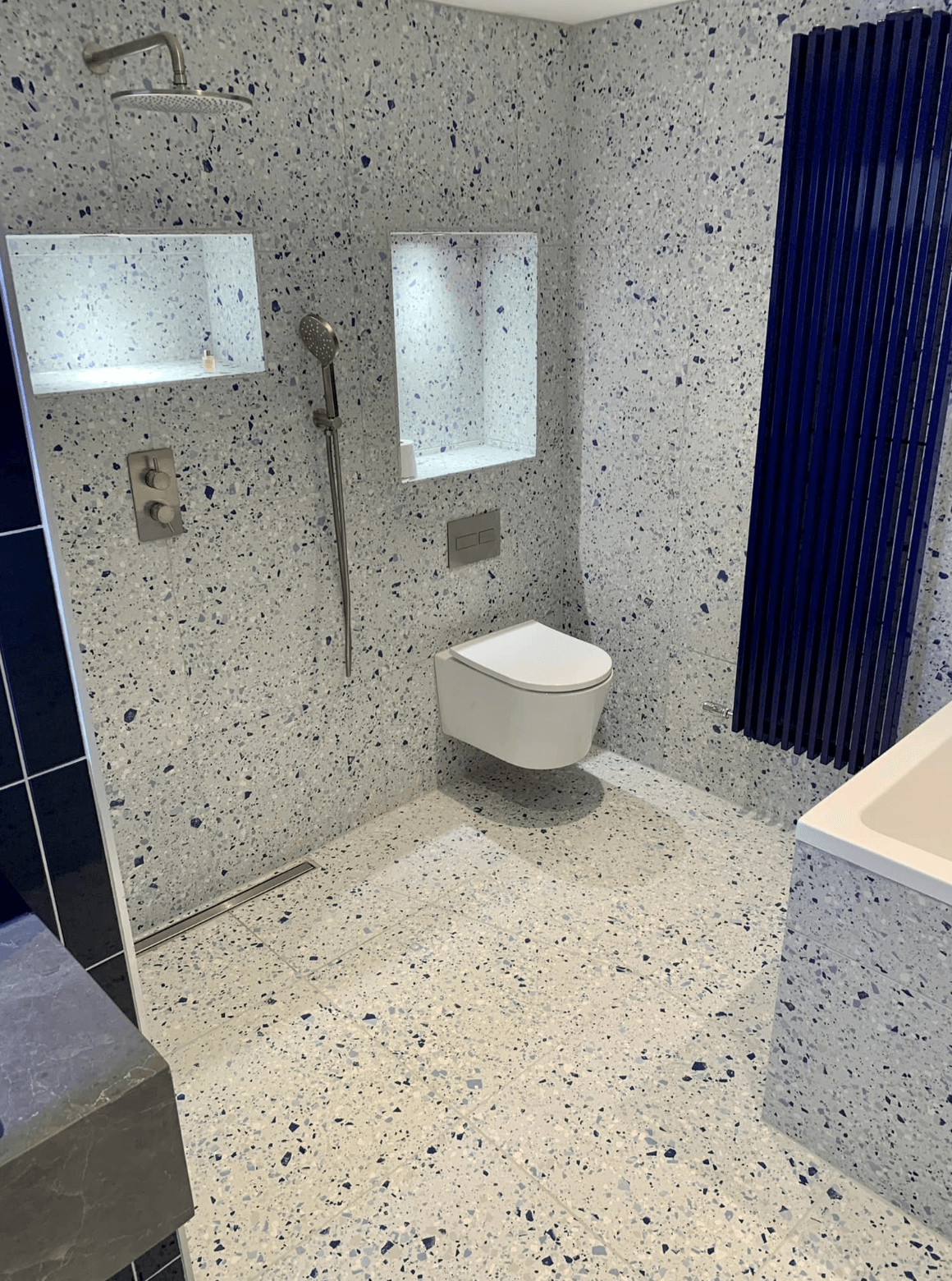 Modern bathroom with speckled tile, wall-mounted toilet, blue shower curtain, and vanity edge