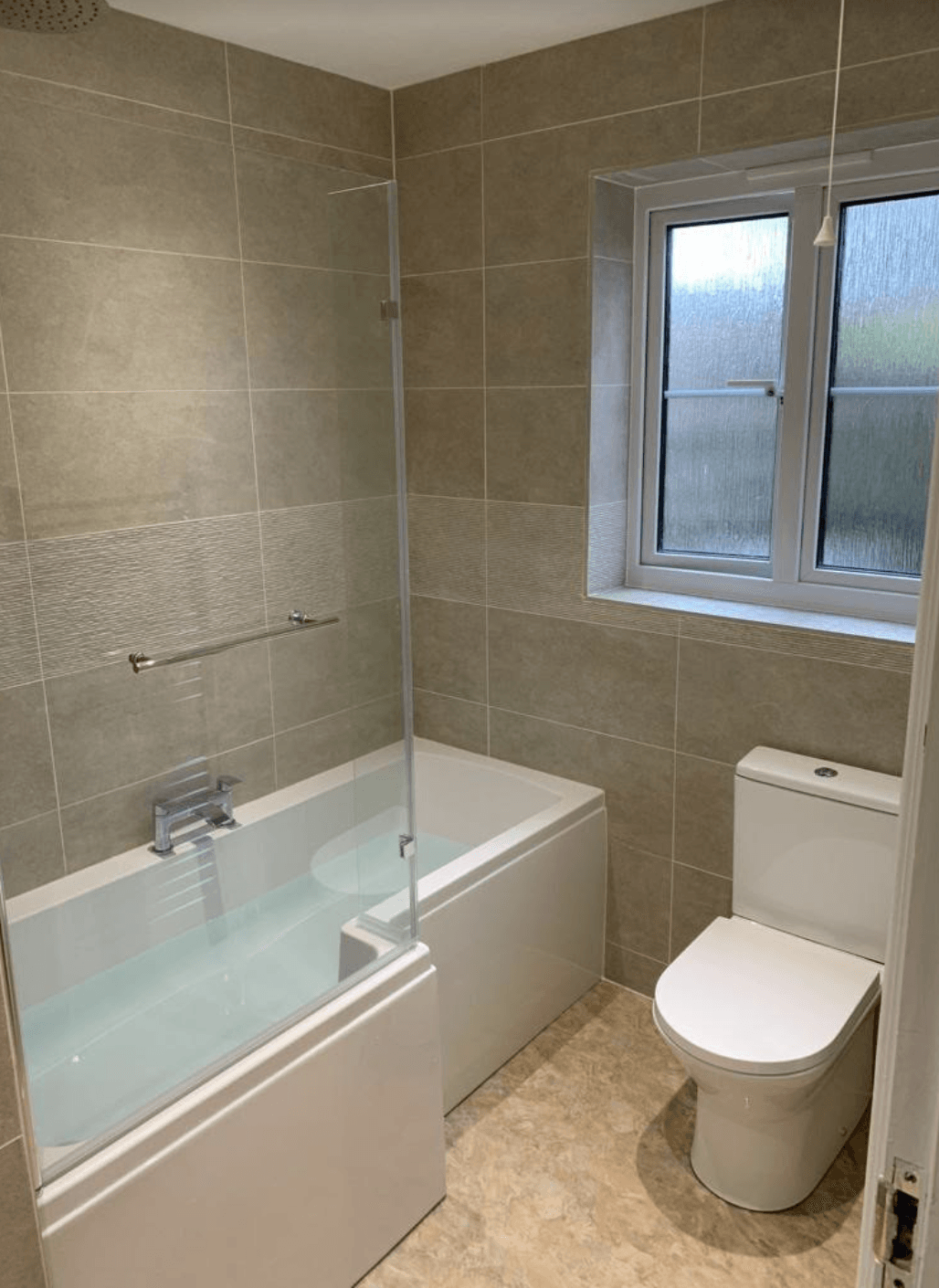 Small tiled bathroom with a bathtub, toilet, and frosted window.