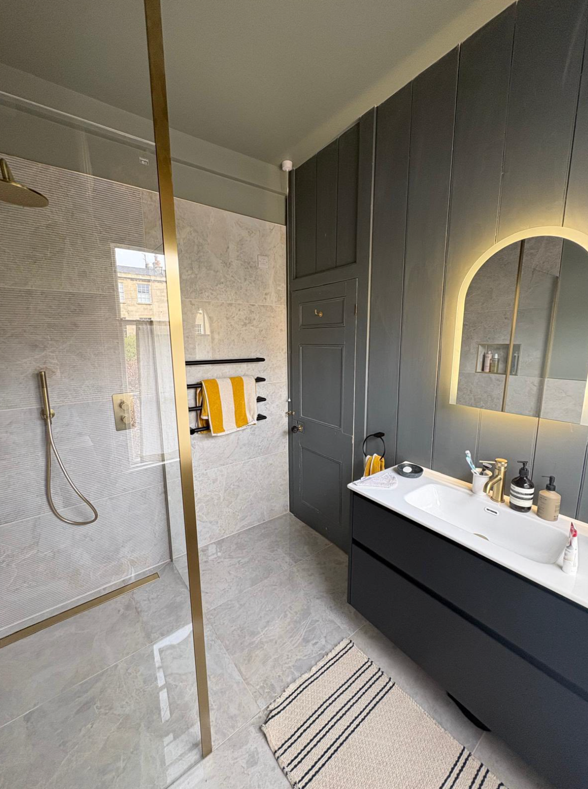 Modern bathroom with walk-in shower, dark vanity, and lit round mirror.