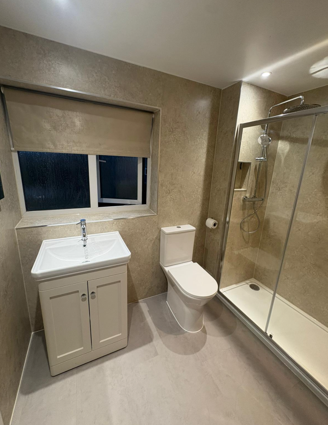 Small modern bathroom with sink, toilet, and glass-enclosed shower in beige tones