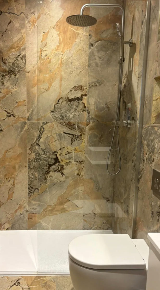 Modern bathroom with stone shower wall, rainfall showerhead, and white toilet seat in the foreground