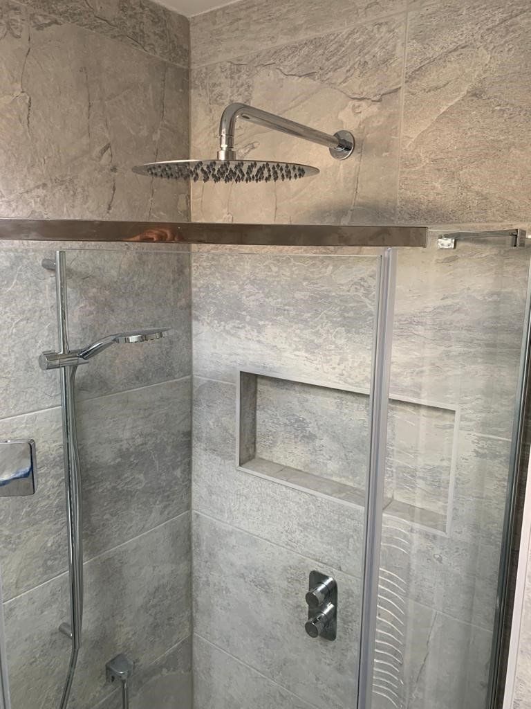 Modern walk-in shower with stone tile, glass door, and built-in shelf under a rain showerhead