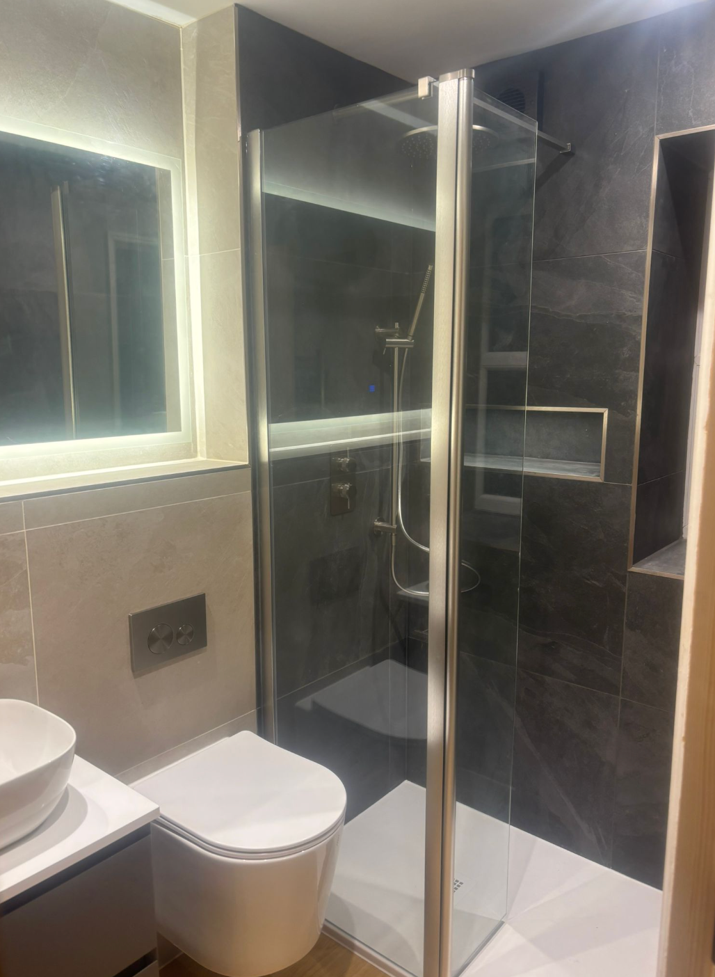 Modern bathroom with a toilet, glass shower enclosure, wall mirror, and vanity sink.