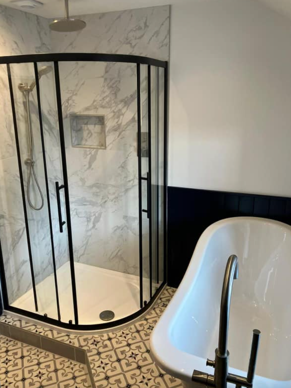 Bathroom with black-framed glass shower and white freestanding bathtub on beige tile floor