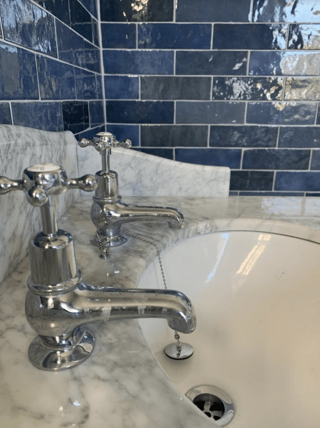 Bathroom sink with chrome faucet and blue subway tile backsplash, marble counter, and white basin