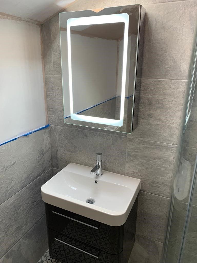 Small tiled bathroom with wall mirror, sink, and black vanity under a bright light.