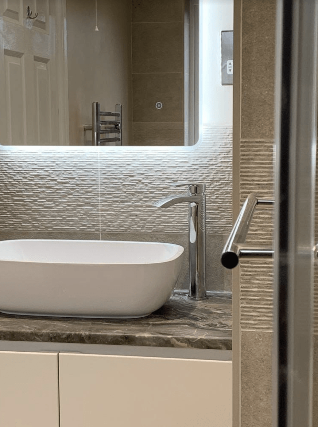 Modern bathroom vanity with white vessel sink, stone countertop, mirror, and beige tiled walls