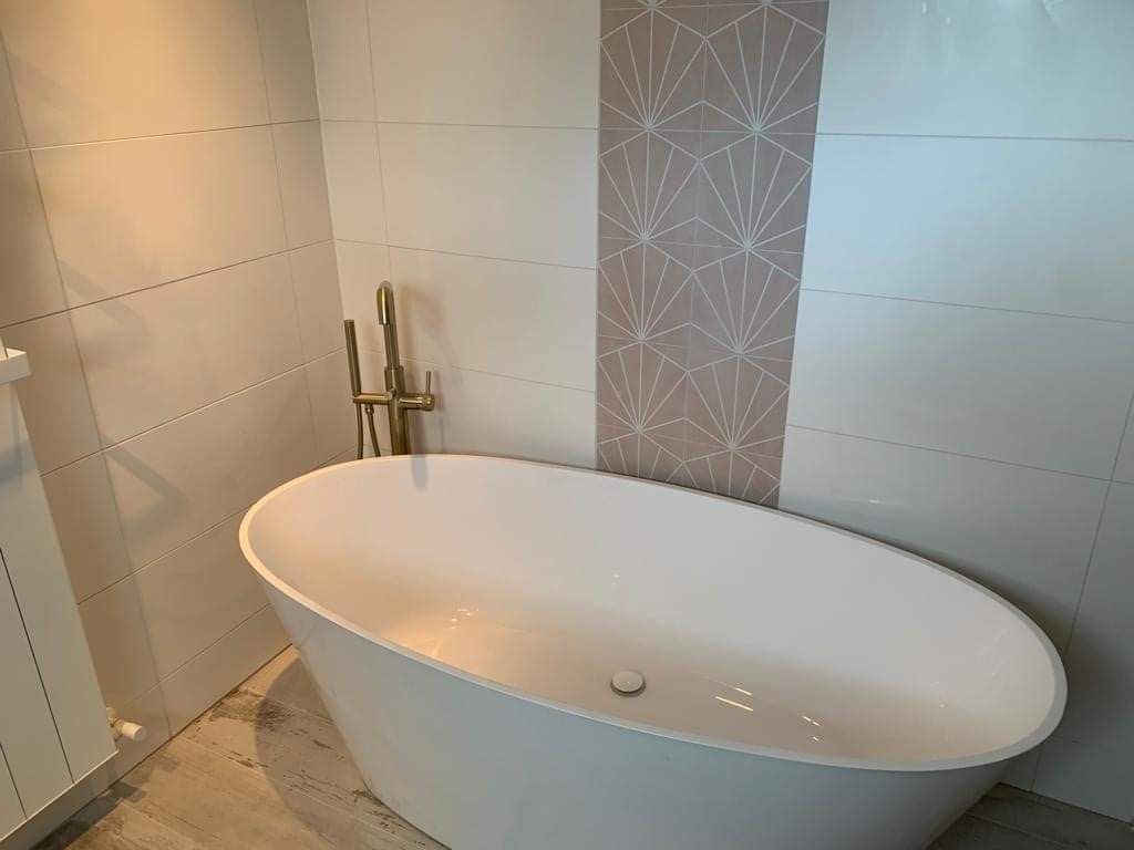 Modern bathroom with a white freestanding oval bathtub beside a tiled wall and patterned accent strip