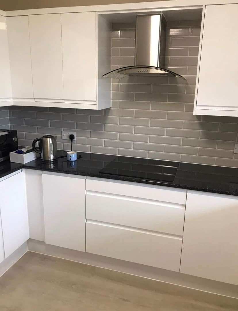 Modern white kitchen with black countertops, gray subway tile backsplash, and stainless steel range hood.