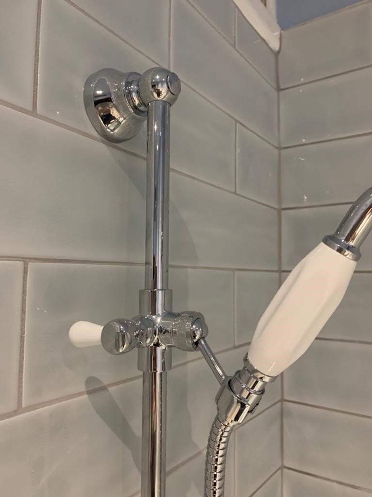 Chrome handheld showerhead mounted on a tiled bathroom wall with a grab bar