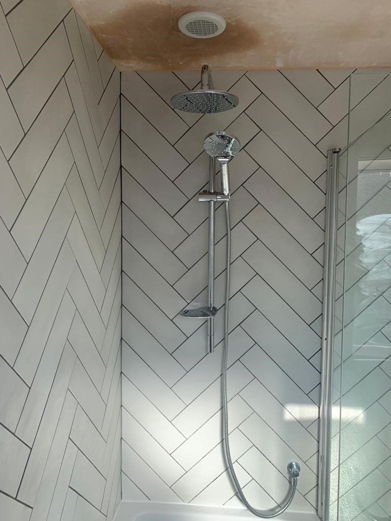 Modern tiled shower with chrome showerhead and handheld sprayer.