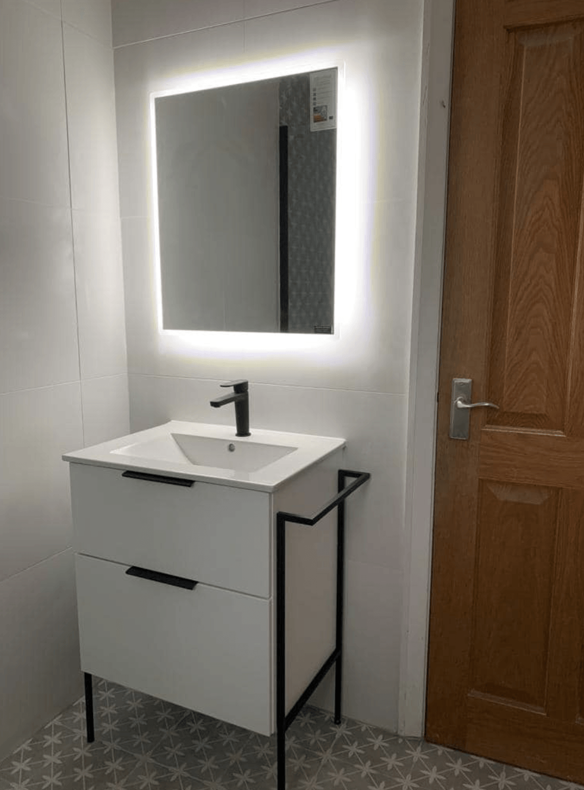 Modern white bathroom vanity with illuminated mirror and wooden door