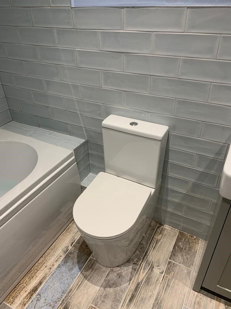 Modern bathroom with white toilet beside a bathtub and gray tiled wall