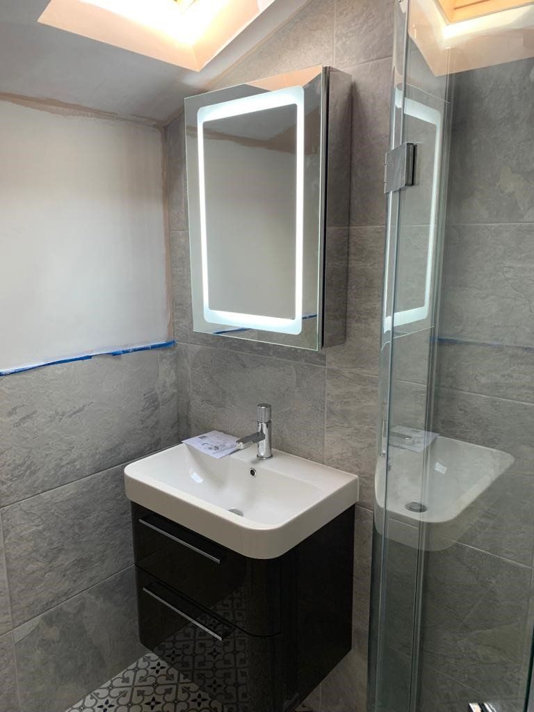 Compact modern bathroom with sink, mirror cabinet, toilet, and glass shower enclosure.