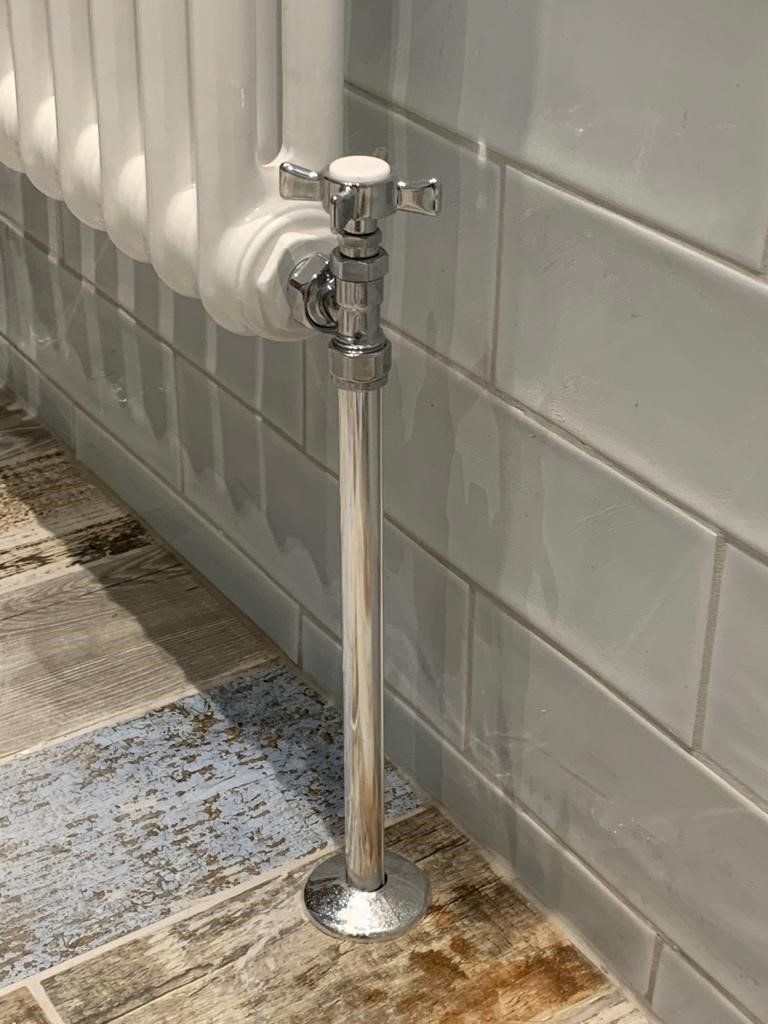 Chrome plumbing pipe with a valve beside a tiled wall and radiator in a restroom-like area