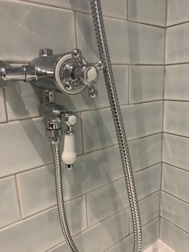 Shower faucet with handheld showerhead and chain on a tiled bathroom wall