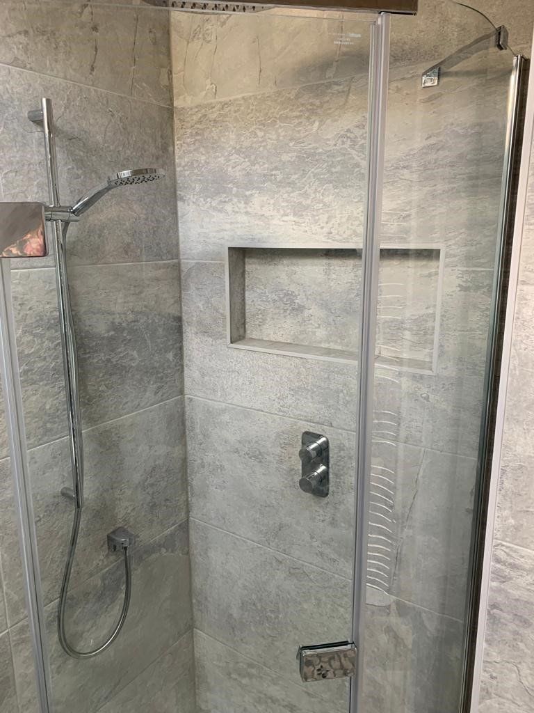 Modern gray tiled walk-in shower with glass door, wall niche, and chrome fixtures