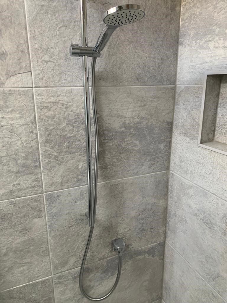 Stainless steel handheld shower with hose mounted on gray tiled bathroom wall